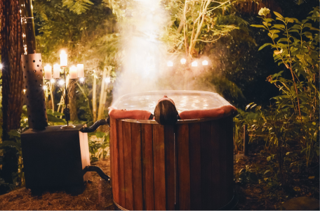 person sitting in a hot tub in the bush with candles lit in the surrounding